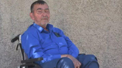 Tekerlekli sandalye kullanıcısı engelli birey Ali Osman Demir, tekerlekli sandalyesinin üzerinde duvar kenarında bir yerde duruyor.