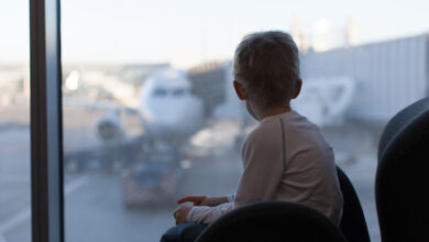 Bir çocuk havaalanında uçağı bekleme salonunda camın arkasından uçuş için hazırlanan bir uçağı izliyor.