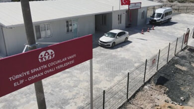 Fotoğrafta tek katlı bir binanın önünde bir minibüs var. Binaya girmek için geçilmesi gereken çevresi tel örgülerle çevrili ek kapının üstünde ise “Türkiye Spastik Çocuklar Vakfı Elif-Osman Ovalı Yerleşkesi” yazıyor.