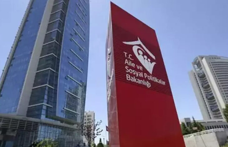 Fotoğrafta, bir gökdelenin yanında kırmızı renkli dikey bir tabela var. Tabelanın üzerinde “T.C. Aile ve Sosyal Hizmetler Bakanlığı” yazıyor.