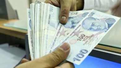 Fotoğrafta, iki kişinin sadece kolları var. Beyaz renkli gömlek benzeri bir şey giymiş olan kişi 100 TL'den oluşan kağıt paraları açık bir şekilde karşı tarafa uzatıyor. Karşı taraftaki kişi paranın diğer ucundan tutuyor.