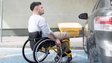 Tekerlekli sandalye kullanılan engelli birey, siyah bir otomobilin sürücü koltuğu kapısına doğru yaklaşıyor.