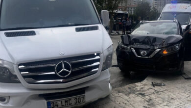 Beyaz bir minibüs ve siyah bir otomobil ön taraftan birbirleriyle çarpışmışlar. Siyah otomobilin ön tarafı içeriye doğru girmiş ve kaput kapağı kırılmış.