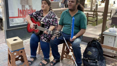 Görme engelli çift Mahdi Saadet ve Zeynep Salehi, plastik sandalye üzerinde oturarak gitar ve melodika çalıp, şarkı söylüyorlar.