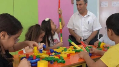 Görme engelli öğretmen Mehmet Yıldız, anaokuluna gelen öğrencileriyle sınıfta ilgileniyor. Öğrenciler çeşitli parçaları olan bir plastik yapboz benzeri oyunda bazı geometrik şekilleri yapıyor.