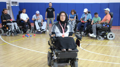 Akülü tekerlekli sandalyeler üzerinde oturan engelli bireyler fotoğrafta var. Akülü tekerlekli sandalyesi ile diğer engelli bireylerin biraz daha önünde duran Lütfiye Uğurlu boynunda kazanmış olduğu gümüş madalya asılı.