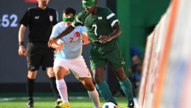 Yeşil renkli forma giyen Brezilya oyuncusu, turkuaz renkli forma giyen Türkiye'nin oyuncusu ve iki futbolcunun arkasında siyah renkli forma giyen hakem var.