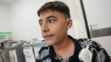 Ahmet Yasin Göçlü, kulağının yan tarafından içeriye doğru uzanan biyonik kulağın kablosu gidiyor ve biyonik kulak cihazı omuzunda duruyor.