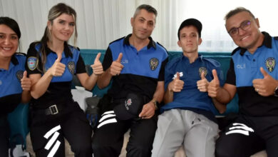 Zihinsel engelli birey Caner Torlak, iki kadın ve iki erkek polis memurunun arasında koltuk üzerinde oturuyor ve baş parmağını yukarı doğru kaldırarak mutluluğunu gösteriyor.