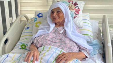 Gülten Saruhan, hasta yatağında oturuyor ve çerçevesindeki insanlara gülümserek bakıyor.