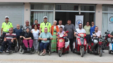Tekerlekli sandalye kullanıcısı ve üç tekerli engelli aracı kullanan bireyler, yan yana duruyorlar. Engelli bireylerin arasında üniforma giymiş trafik polisleri de var.