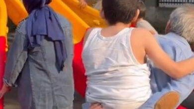 Bir adamın sırtında taşıdığı küçük çocuk, çocuk oyun parkında oynayan akranlarını seyrediyor.