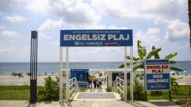 Fotoğrafta, plaja doğru inilen bir alan var. Plaja giriş yapılan bölümde üst tarafta ve fotoğrafın sağında engelsiz plaj yazılarının olduğu tabelalar var.