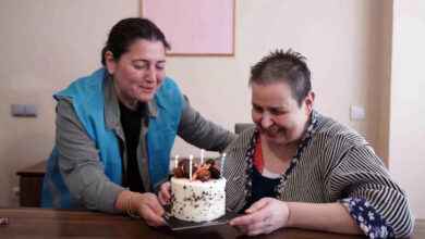 Görme engelli birey Canan Canbakan'ın doğum gününü kutlamak için beyaz renkli bir yaş pastayı masanın üzerine katıyorlar.