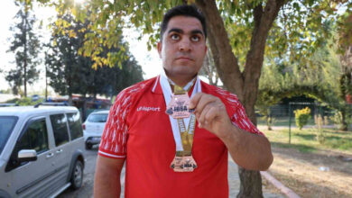 Fotoğrafta, görme engelli milli halterci Ayhan Kaya, bir cadde üzerinde boynunda Görme Engelliler Dünya Halter Şampiyonası'nda kazandığı üçüncülük madalyası var.