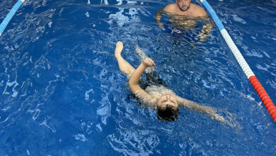 Havuzun içerisinde yüzen engelli birey ve biraz geride duran babası, çocuğunu izliyor.