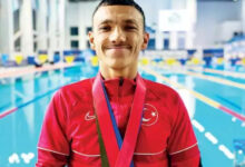 Paralimpik sporcu Umut Ünlü, havuzun kenarında boynundaki madalya ile birlikte fotoğraf için poz veriyor.