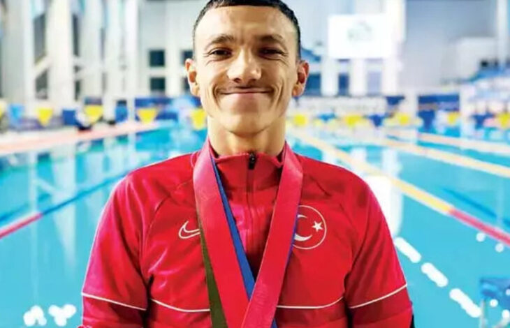 Paralimpik sporcu Umut Ünlü, havuzun kenarında boynundaki madalya ile birlikte fotoğraf için poz veriyor.