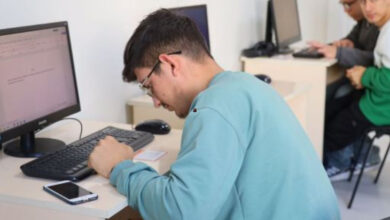 Bilgisayar başında oturan görme engelli birey, klavye tuşlarını daha rahat görebilmek için öne doğru biraz eğilmiş. Diğer bilgisayarlarda da engelli bireyler oturarak, kullanıyorlar.