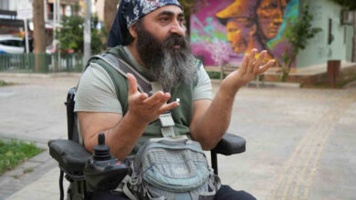 Akülü tekerlekli sandalye kullanıcısı engelli birey Tanju Mete, kollarını hafif yukarı doğru kaldırıp, avuç içi yukarı bakacak şekilde tutarak olayı basına anlatıyor.