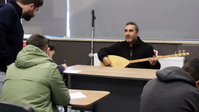 Görme engelli müzik öğretmeni Süleyman Ekici, öğretmen masasının arkasında oturarak saz çalıyor. Karşısında ise öğrencileri deftere not alıyor.