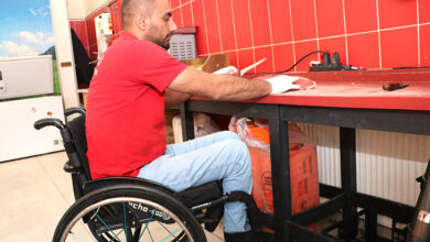 Tekerlekli sandalye kullanıcısı engelli birey Sabahattin Demirtaş, et kesme tezgahına yaklaşarak elindeki bıçakla et doğrama işlemi yapıyor.