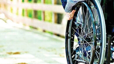 Fotoğrafta, tekerlekli sandalye kullanan engelli birey belden aşağısı gözüküyor. Tekerlekli sandalyenin tekerlerinden iterek hareket edebiliyor.