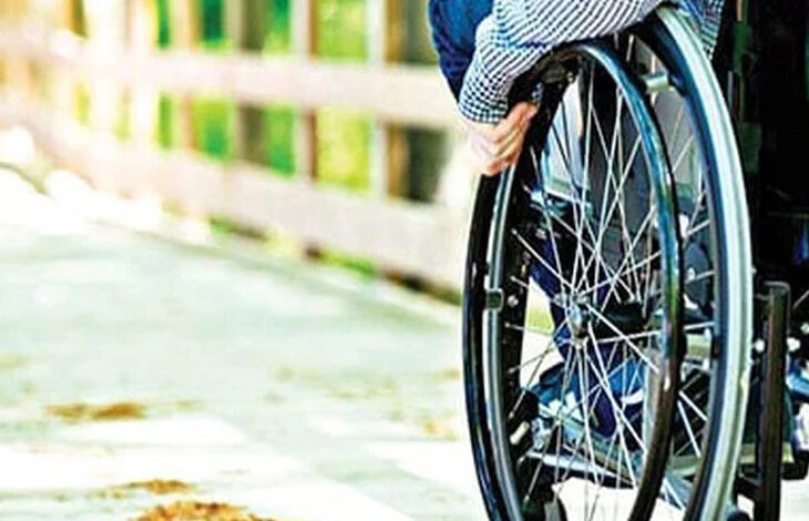 Fotoğrafta, tekerlekli sandalye kullanan engelli birey belden aşağısı gözüküyor. Tekerlekli sandalyenin tekerlerinden iterek hareket edebiliyor.