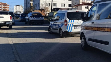 Fotoğrafta, bir sokakta park halinde olan birçok otomobil var. Park halinde olan otomobillerin bazıları polis aracı ve arka arkaya üç polis aracı yolun kenarında duruyor.