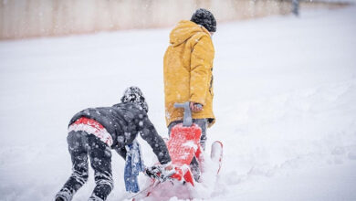 Kar yağışının olduğu bir yerde bir çocuk ve ebeveyni ile birlikte kayak yaptıkları eşyaları yerden sürükleyerek taşıyorlar.