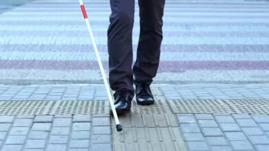 Fotoğrafta, görme engelli bireyler için yapılmış sarı renkli rehber yol var. Görme engelli birey elindeki beyaz baston ile rehber yolu takip ediyor.