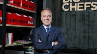Fotoğrafta, BigChefs CEO’su Altan Kosova markanın kutularının sıralı olduğu bir açık dolabının önünde ve arkasına kasa masasını alarak ellerini birleştirmiş şekilde ayakta duruyor.