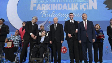 Fotoğrafta, tekerlekli sandalye kullanan engelli bireyler ve MHP Genel Başkanı Devlet Bahçeli kürsüde plaket ve hediye takdimini gerçekleştiriyor.