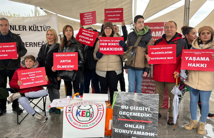 KEDİ -Kabul, Eşitlik, Dahil olma, İstihdam- Otizm Derneği Yönetim Kurulu Başkanı Serap Dikmen ve engelli bireyler ile aileleri ellerinde yazıların olduğu pankartları tutuyorlar.