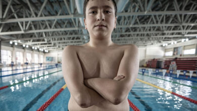 Fotoğraf, bir yüzme havuzunun kenarında duran genç bir sporcuyu göstermektedir. 15 yaşında olduğu belirtilen çocuk, doğuştan kolları ve ayakları olmamasına rağmen kararlı bir duruş sergiliyor. Geniş bir açıyla çekilen bu karede, çocuğun çıplak üst vücudu, güçlü duruşu ve kendine güveni ön planda. Arkada modern bir yüzme havuzu, mavi su, renkli kulvar ayırıcıları ve çelik konstrüksiyon çatı dikkat çekiyor. Çocuğun yüzündeki ciddi ifade, azim ve kararlılığı yansıtıyor. Bu sahne, fiziksel engellerin aşılabileceğini ve spora olan tutkuyu güçlü bir şekilde simgeliyor.