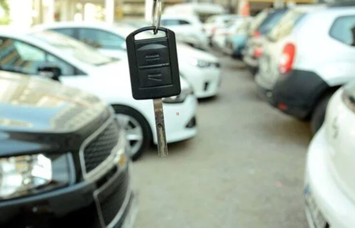 Fotoğrafta, bir araba galerisinde yan yana duran iki sıra halinde otomobiller var. Fotoğrafı çeken kameranın tam önünde ise bir otomobil anahtarı yukarıdan aşağıya doğru sallanarak duruyor.