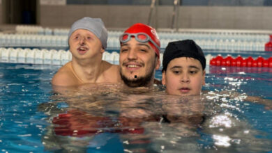 Yüzme eğitimi alan iki engelli çocuk ve eğitmen havuz içerisinde yüzüyorlar.