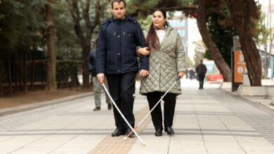 Fotoğrafta, görme engelli çift Hüseyin Özkan ve Yeter Özkan ellerindeki beyaz bastonla bir yolda yürüyüş yapıyorlar.