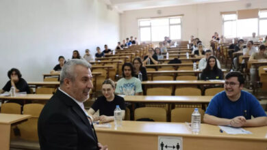 Fotoğrafta, bir üniversitenin sınıfında öğrenciler ve öğrencilerin önündeki boş alanda ders anlatan bir üniversite hocası var.