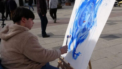 Fotoğrafta, engelli birey Enes Kürekçi bir tablo resmediyor. Resim mavi renkle çizilmiş bir kadının yüzü ve kırmızı renkli dudağa sahip olarak resmedilmiş.