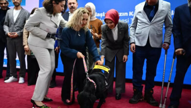 Fotoğrafta, Aile ve Sosyal Hizmetler Bakanı Mahinur Özdemir Göktaş, Görme engelli bir bireyin rehber köpeğini seviyor. Göktaş'ın çevresinde baston ile ayakta duran başka engelli bireyler ve bir eli protez olan engelli bir kadında sahnede yer alan köpeğin yakınında ayakta duruyor.