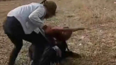 Görselde, açık bir arazide iki kişi arasında fiziksel bir saldırı yaşandığı görülüyor. Başörtülü bir kadın, yerde yatan bir kişiye sopa ile vuruyor. Saldırıya uğrayan kişi savunmasız bir şekilde yere düşmüş durumda. Çevrede kimse görünmüyor ve olay kırsal bir alanda geçiyor.