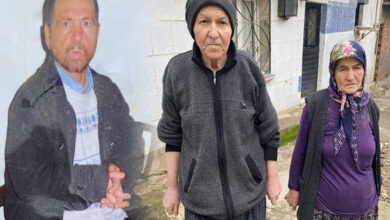 Görselde, yaşlı bir adam ve kadın bir köy ortamında, taş ve toprak yolda duruyor. Adam koyu renkli bir eşofman takımı ve bere giymiş, yüzü ciddi ve yorgun görünüyor. Yanındaki kadın mor tonlarında bir kıyafet ve başörtüsü takıyor. Arka planda, mavi-beyaz duvarlı bir ev görülüyor. Sol tarafta, adamın gençlik haline ait olduğu düşünülen soluk bir fotoğraf montajı bulunuyor.