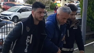 Görselde, polis ekipleri kelepçeli bir adamı kolluk kuvvetleri eşliğinde adliyeye veya karakola götürüyor. Adam koyu renkli bir mont giymiş ve başı öne eğik durumda. Polis memurları "POLİS" yazılı yelekler giymiş ve güvenlik önlemleri almış. Arka planda ise araçlar ve şehir ortamı görülüyor.