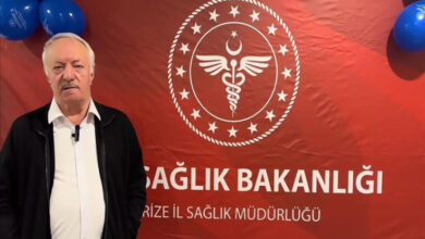 Kanseri yenen emekli öğretmen Yakup Cansız, Sağlık Bakanlığı logosu önünde poz veriyor.