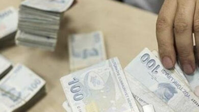 Görselde, bir masa üzerinde Türk Lirası banknotları bulunuyor. Elleri görünen bir kişi, 100 TL’lik banknotları sayıyor ve desteler halinde tutuyor. Masanın üzerinde de banknotlar dağınık halde duruyor. Görüntü, nakit para sayımı veya ödeme işlemi yapıldığı izlenimini veriyor.