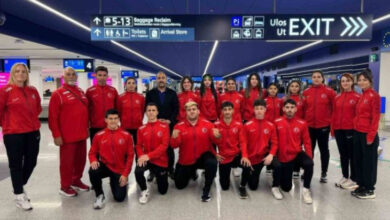 Görselde, havaalanında çekilmiş bir grup fotoğrafı yer alıyor. Türkiye'yi temsil eden, kırmızı eşofman giyen özel sporcular ve antrenörleri birlikte poz veriyor. Üstlerindeki Türk bayrağı logosu, onların milli takım mensubu olduğunu gösteriyor. Arka planda havaalanı yön tabelaları ve çıkış işaretleri bulunuyor. Grup, enerjik ve motive görünüyor, muhtemelen bir yarışma veya organizasyon için seyahate hazırlanıyorlar.