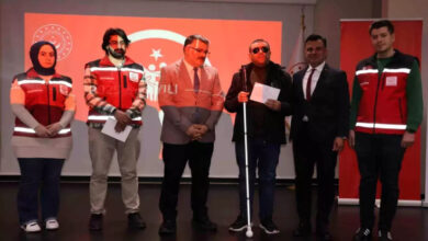 Kürsüde yetkililer ve görme engelli gazi erkek bulunuyor.