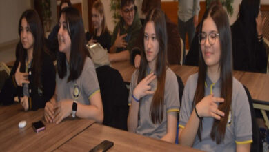 Sıralarda oturan öğrenciler elleriyle işaret dili sembolü kullanıyor.