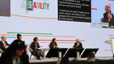 Aile ve Sosyal Hizmetler Bakanı Mahinur Özdemir Göktaş, konuşma koltuğunda oturarak elindeki mikrofonla konuşma yapıyor ve diğer konuşmacılar da sahnede bulunuyor.